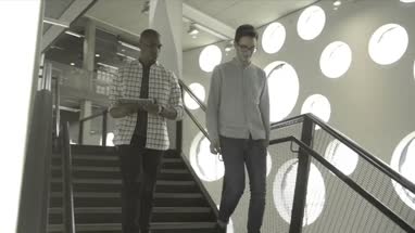 Men holding digital tablet and having discussion while walking in office lobby
