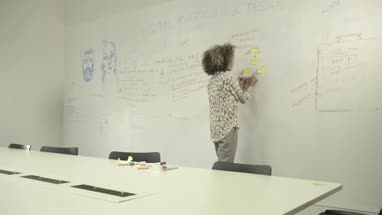 Young woman sticking adhesive note on notice board in office