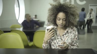 Young woman drinking and using smart phone in office café