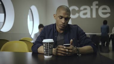 Young man drinking and using mobile phone in office café