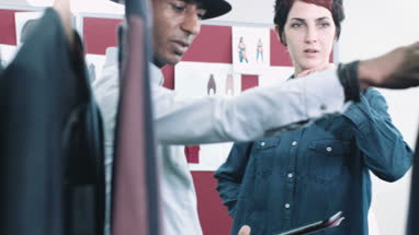 Fashion designers looking at digital tablet and clothes in studio