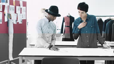 Fashion designers looking at digital tablet and clothes in studio