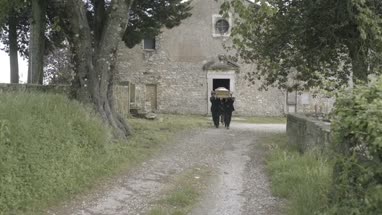 Pallbearers walking to graveyard with coffin followed by family