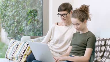 Mom helping teenager with homework on laptop