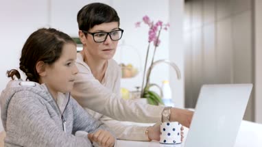 Mom helping daughter on laptop with homework