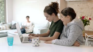 Sisters using laptop together with Mom in background