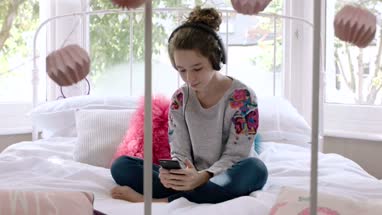 Teenager listening to music on smartphone in bedroom