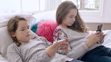Sisters looking at their smartphones in bedroom