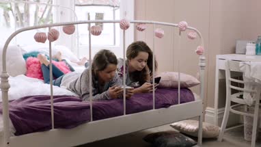 Sisters looking at their smartphones in bedroom