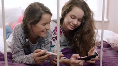 Sisters looking at their smartphones in bedroom