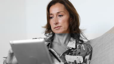 Mature woman at home using digital tablet and credit card