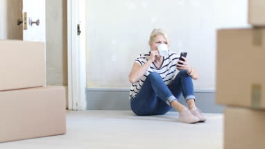 Mature female using smartphone with moving boxes