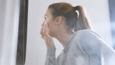 Young adult female looking in mirror examining skin