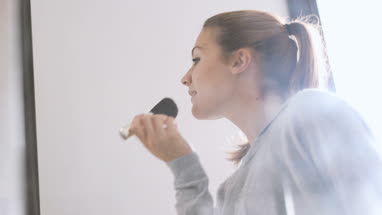 Young adult female looking in mirror putting make-up on 