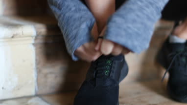 Young adult female tying shoe lace on trainer