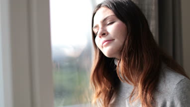 Woman looking out of window and to camera in morning light