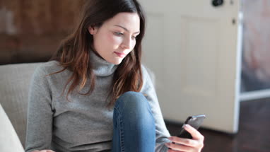 Woman checking smartphone at home on sofa