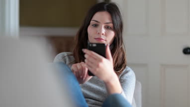 Woman checking smartphone at home on sofa