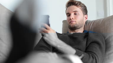 Man checking smartphone at home on sofa