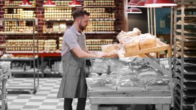 Baker in bakery stocking shelves and looking to camera