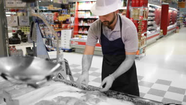 Fishmonger in store arranging fish counter