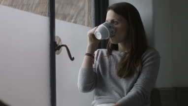 Young adult female having morning coffee and looking out of window