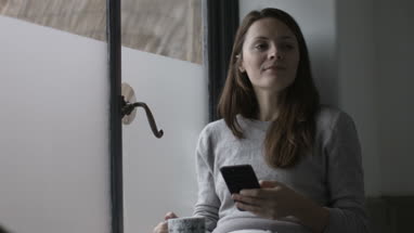 Young adult female having morning coffee and checking smartphone