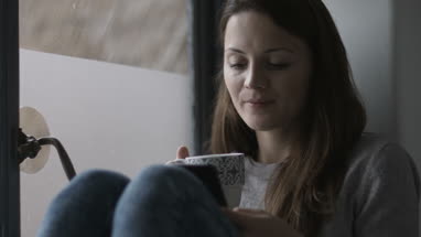 Young adult female having morning coffee and using smartphone
