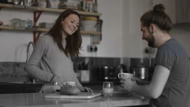Girlfriend passing boyfriend coffee at breakfast