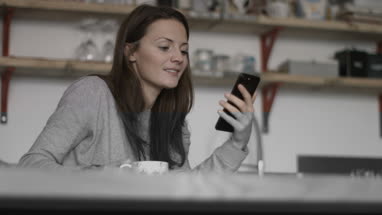 Young adult female having morning coffee and checking smartphone