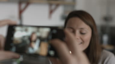 Smartphone taking photo of woman holding cupcake with candle