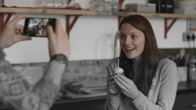 Boyfriend taking photo of girlfriend holding cupcake with candle