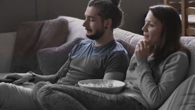 Young couple eating popcorn and watching home movie