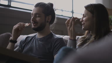 Young couple eating takeout pizza at home