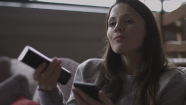 Young adult female watching TV and using smartphone