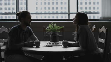 Young adult couple in loft apartment having coffee across table