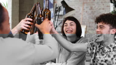 Group of friends clinking beer bottles at a house party
