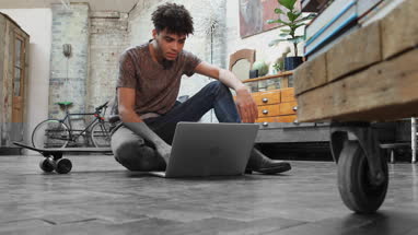 Young adult male sitting on skateboard using laptop