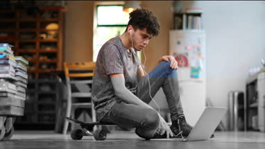 Young adult male sitting on skateboard using laptop