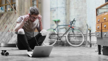 Young adult male sitting on skateboard using laptop