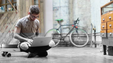 Young adult male sitting on skateboard using laptop