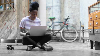 Young adult female sitting on skateboard using laptop
