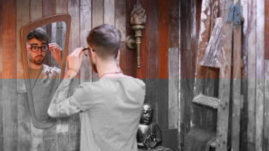 Young adult male putting on reading glasses and looking in mirror