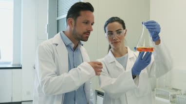 Female scientist analyzing liquid in conical flask with a male colleague