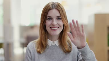 Portrait of female entrepreneur waving to camera in a modern shared workplace