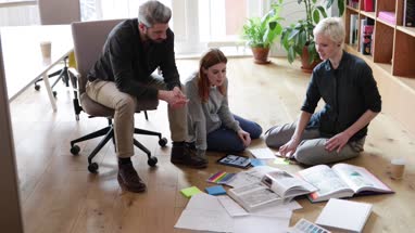 Overhead shot group of designers discussing ideas with paperwork on office floor