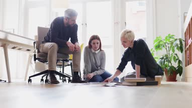 Group of designers discussing ideas with paperwork on office floor