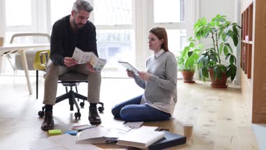 Colleagues discussing ideas with paperwork on office floor