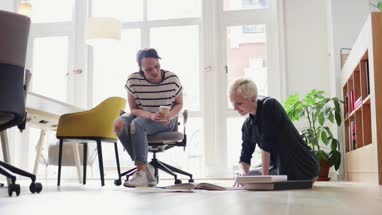 Colleagues discussing ideas with paperwork on office floor