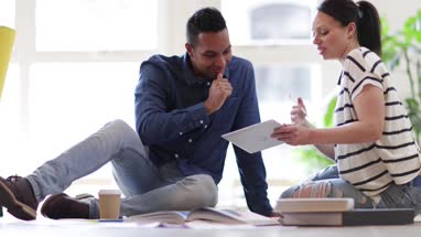 Colleagues working on ideas with digital tablet and paperwork on office floor
